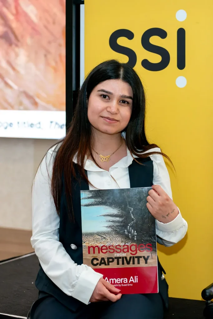 Portrait of Amera Ali holding her book Messages from Captivity at the conference