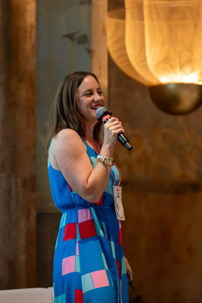 Angela McKenzie speaking on stage at a corporate networking and conference event while holding a microphone