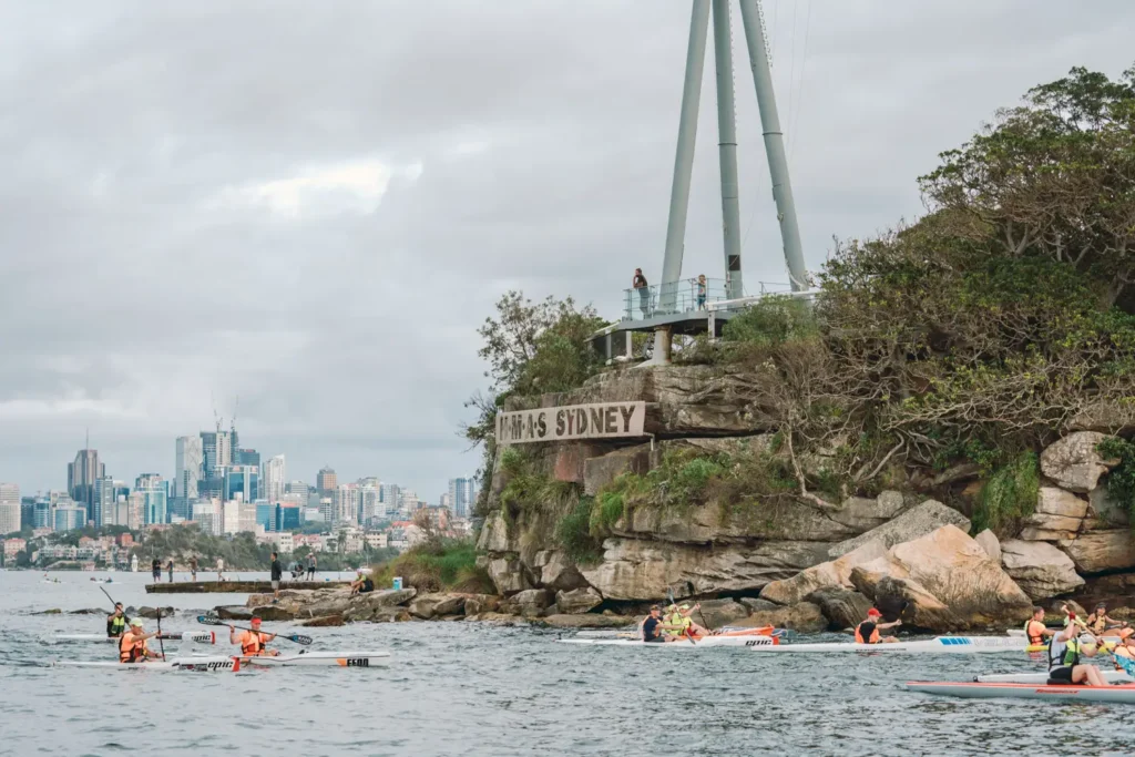Surfski racers passing Bradleys Head with North Sydney skyline visible in the distance