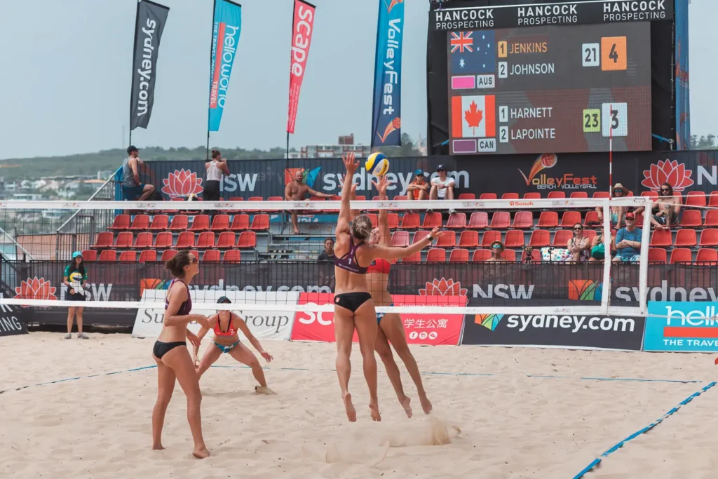Wide shot of a women’s beach volleyball match in Sydney with scoreboard and spectators visible