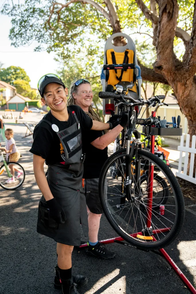 Bicycle repair volunteers posing beside a bike repair stand at a neighbourhood street event