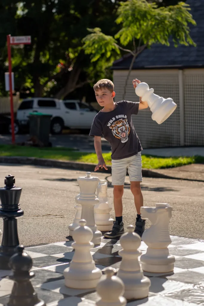 Boy moving oversized chess pieces on a giant outdoor chessboard during a community play day