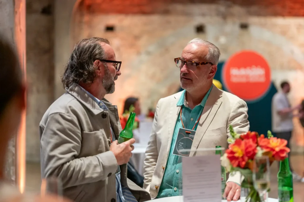 Two attendees having a conversation with drinks during an evening networking event