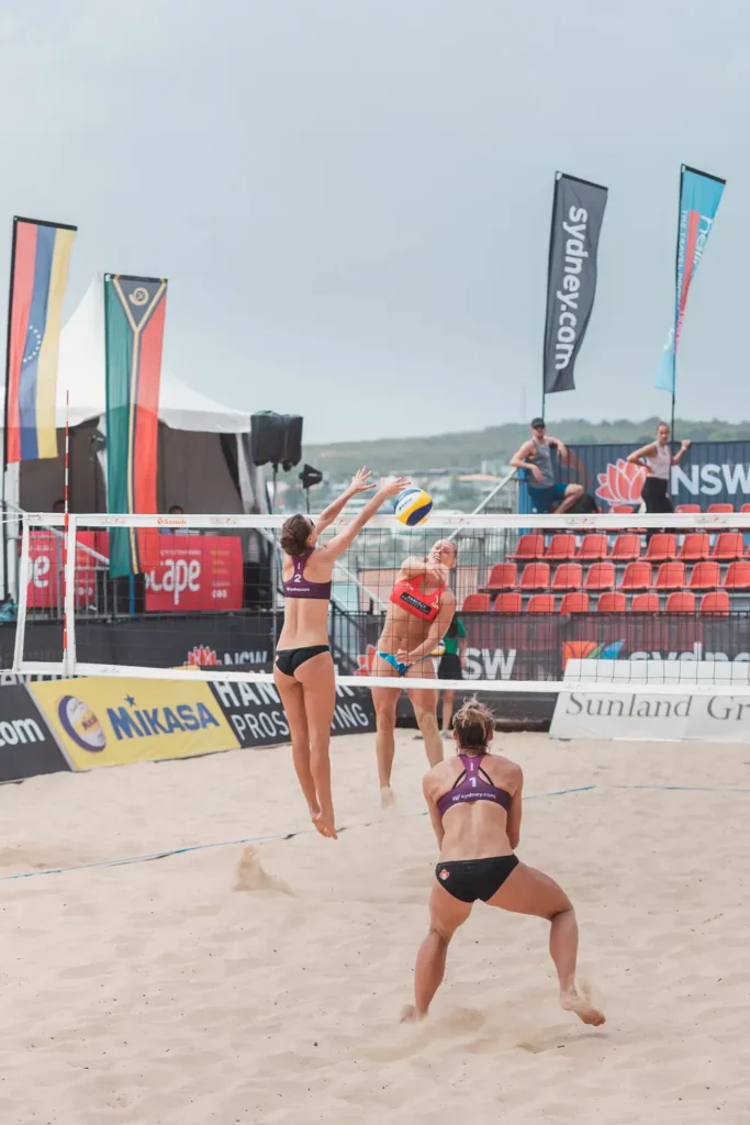 Canadian and Australian teams competing in an active beach volleyball rally near the net