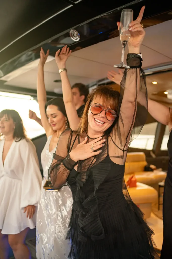 Woman in a black dress raising a champagne glass while celebrating with friends on a luxury yacht