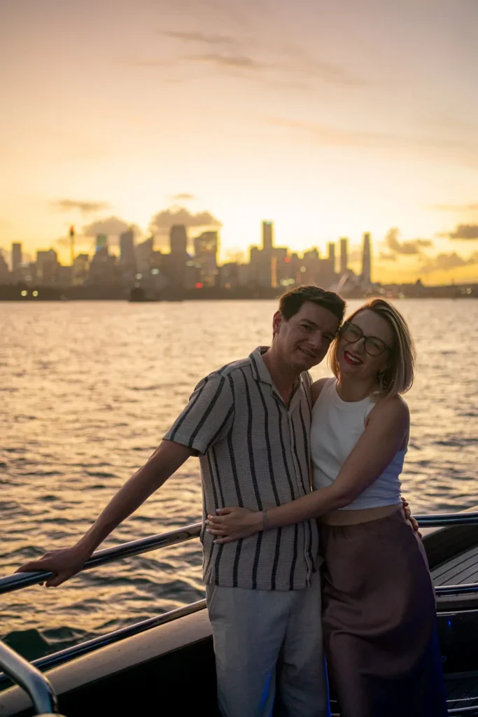 Couple embracing on a yacht with Sydney skyline glowing at sunset