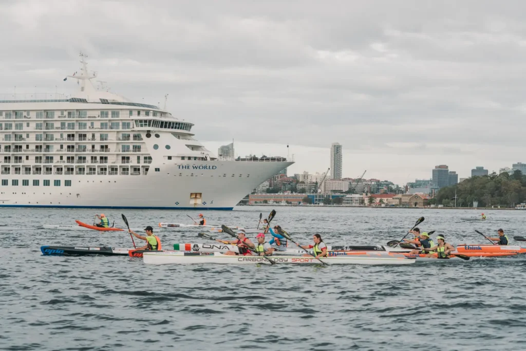 Surfski athletes paddling near a large cruise ship during a Sydney Harbour ocean race