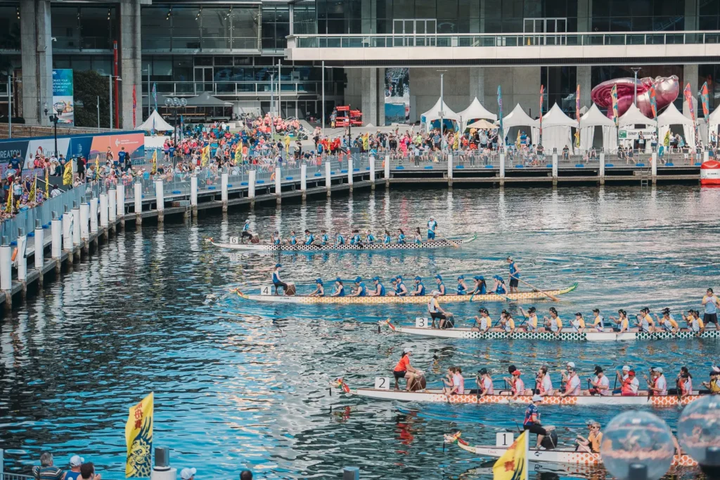 Multiple dragon boat heats racing side by side near festival spectators
