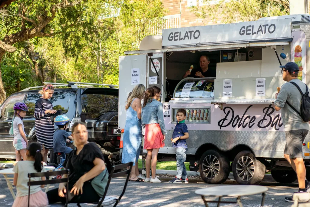 Families lining up at a gelato truck during a sunny suburban community street festival
