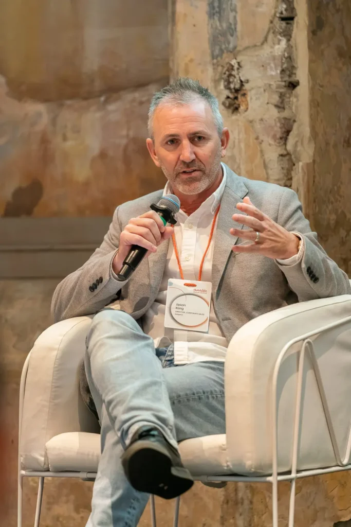 Jason King speaking during a panel discussion at a corporate conference event while holding a microphone