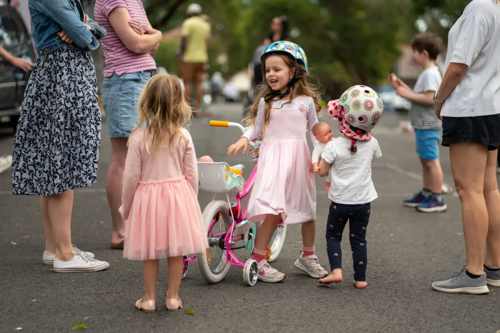 Children chatting and playing around a bicycle during a neighbourhood street gathering