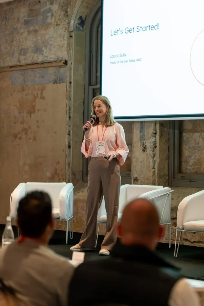 Laura Sully presenting on stage during a corporate conference session with a presentation screen in the background