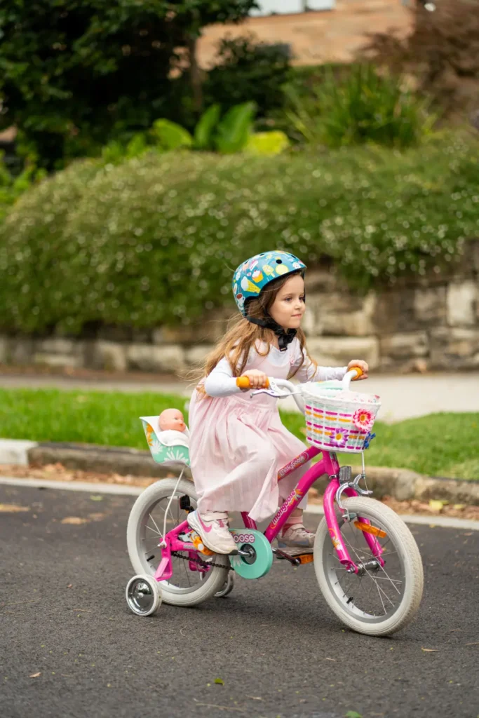 Young girl riding a pink bicycle with a helmet on a quiet suburban street during a community event