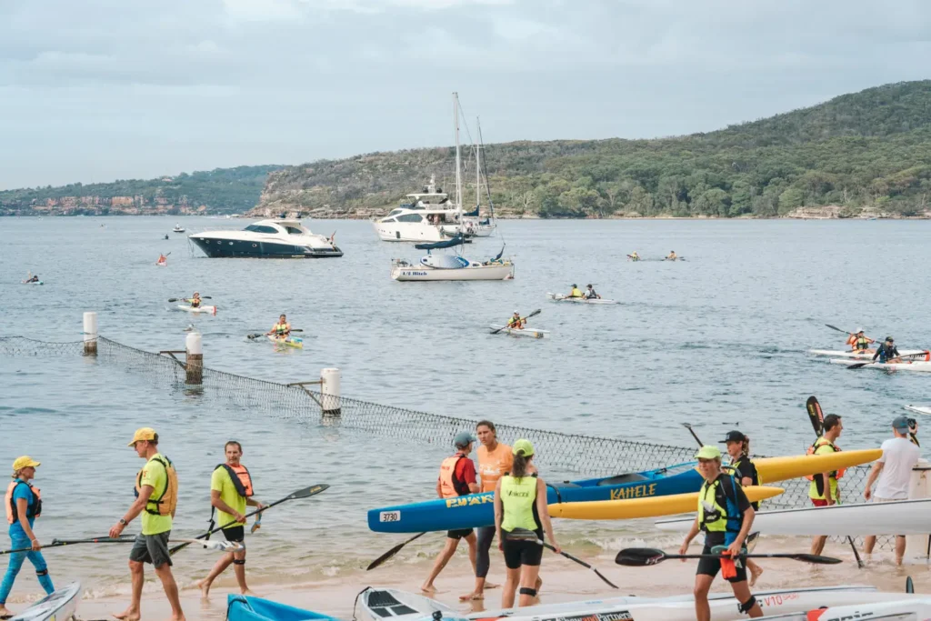 Surfski athletes carrying boats and paddles along the shoreline after the event
