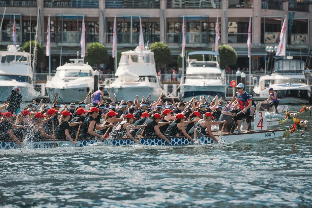 Dragon boat crew in red caps powering through the water during a Sydney harbour race
