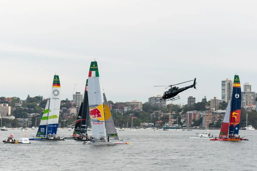 SailGP fleet lineup on Sydney Harbour with a helicopter filming above the racing catamarans