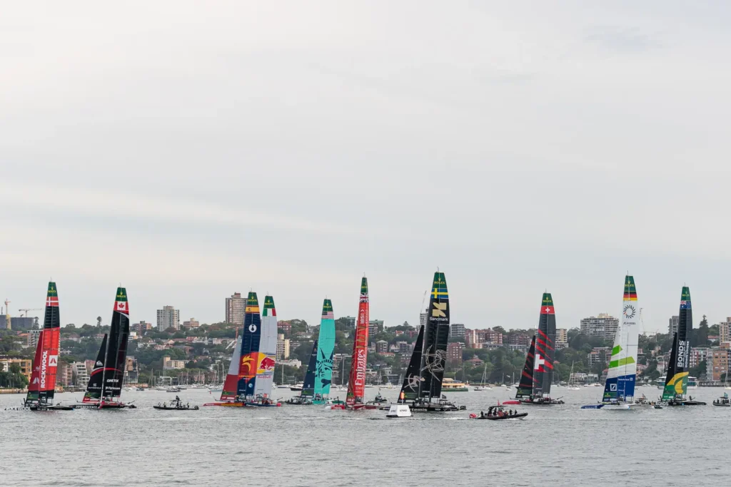 Wide panoramic view of multiple SailGP F50 catamarans gathered on Sydney Harbour during regatta preparations