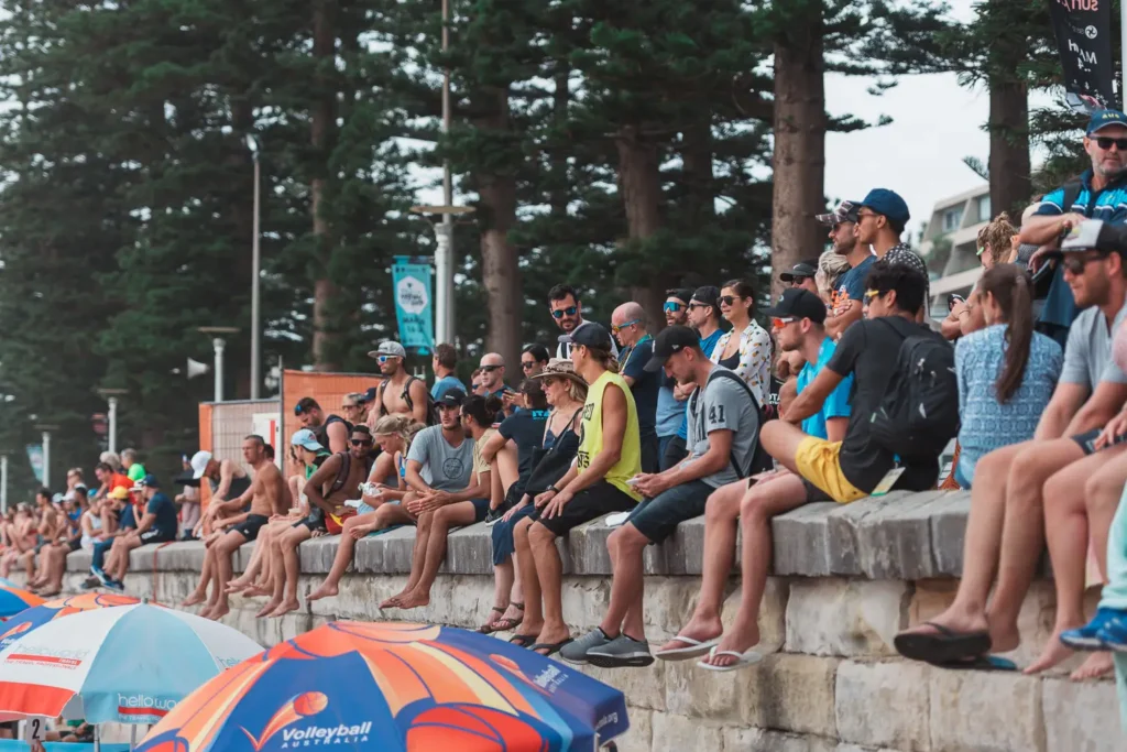 Spectators sitting along the sidelines watching a beach volleyball tournament in Sydney