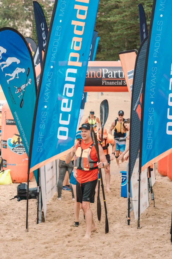 Ocean paddlers walking through sponsor banners after completing the race