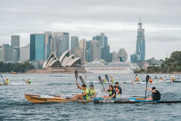 Two surf ski paddlers racing across Sydney Harbour with the Opera House and city skyline behind them