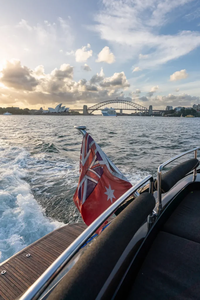 View from a luxury yacht cruising past the Sydney Opera House and Harbour Bridge at sunset