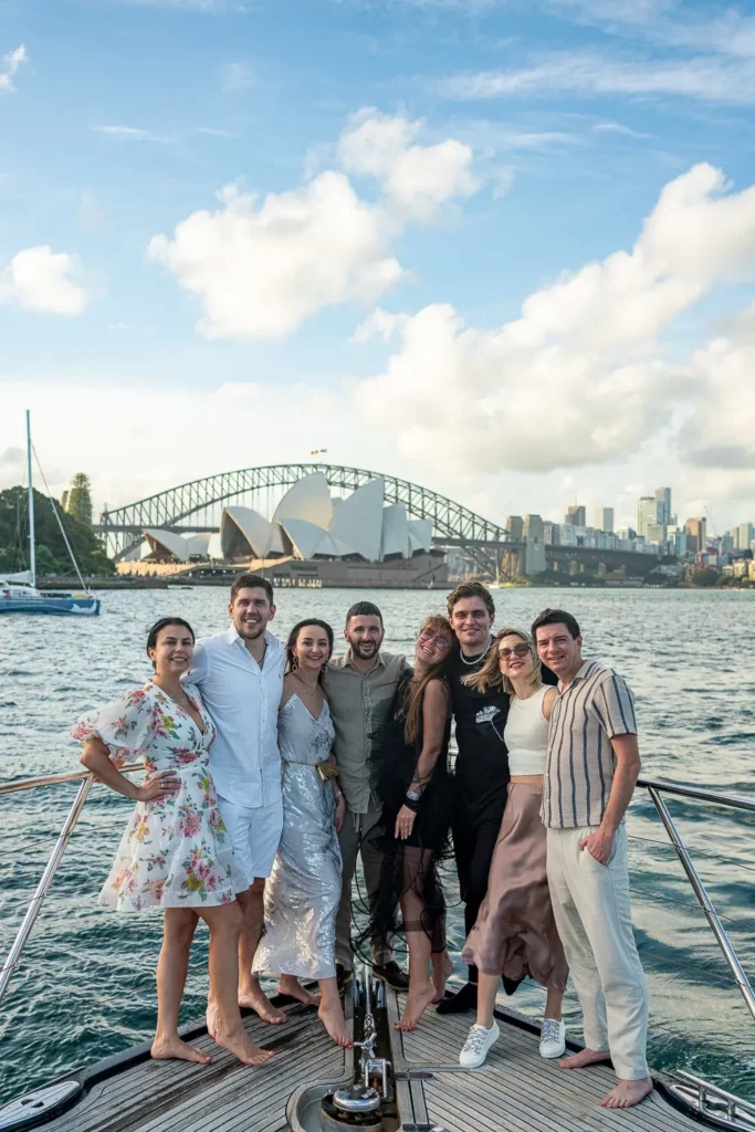 Group of friends posing on the front of a luxury yacht with the Sydney Opera House and Harbour Bridge in the background