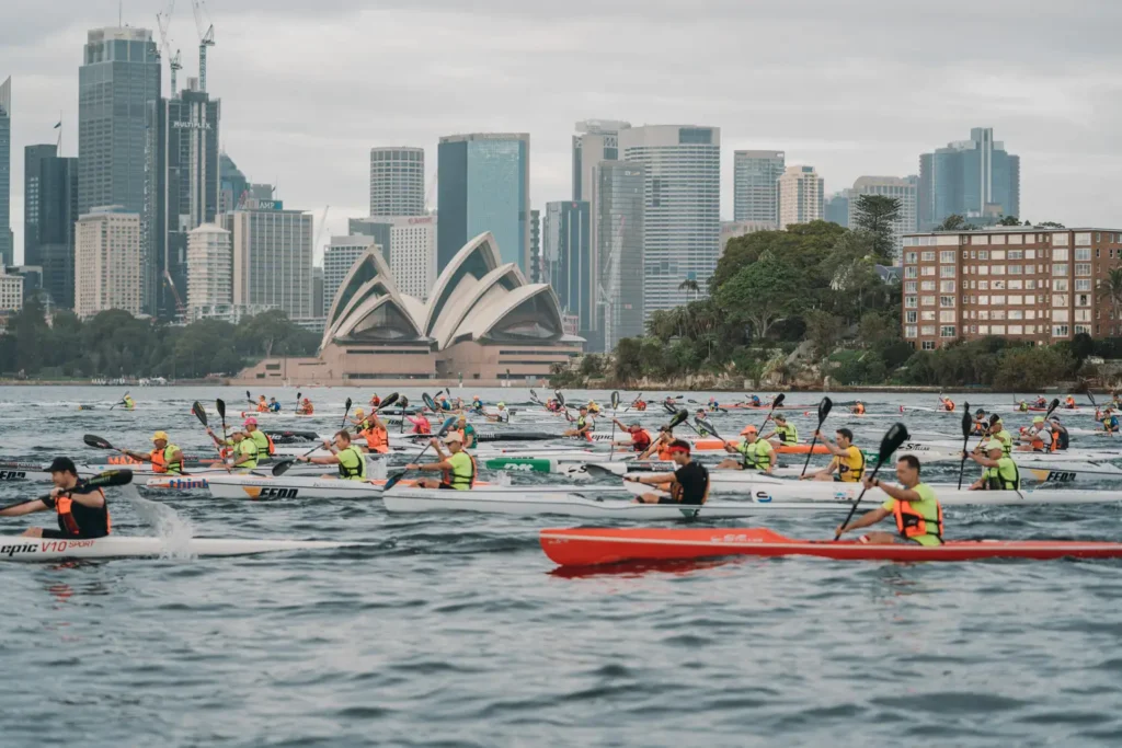 Surfski competitors paddling past the Sydney Opera House with the Sydney skyline in the background