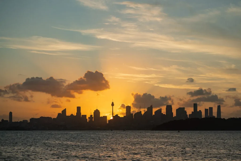 Sydney city skyline silhouetted against a glowing sunset viewed from the harbour