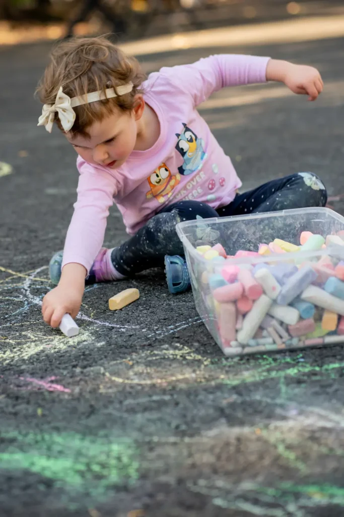 Toddler drawing colourful chalk art on asphalt during a family-friendly outdoor play event