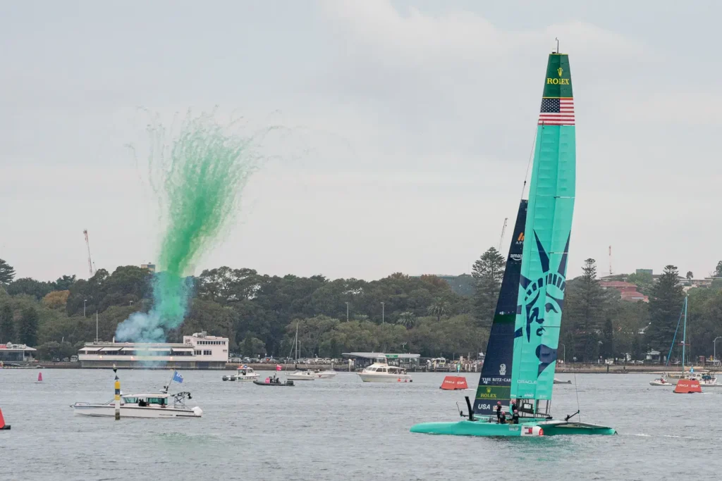 USA SailGP F50 catamaran winning the race and greeted with green smoke effects during a SailGP race in Sydney Harbour