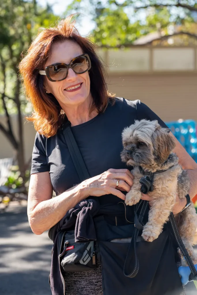 Smiling woman holding a small dog while attending a suburban community street gathering