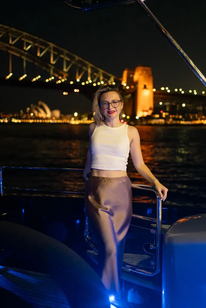 Woman posing on a yacht at night with Sydney Harbour Bridge lights in the background