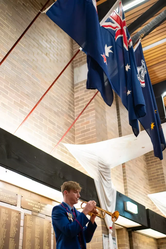 Young bugler playing trumpet beneath Australian flags during memorial ceremony