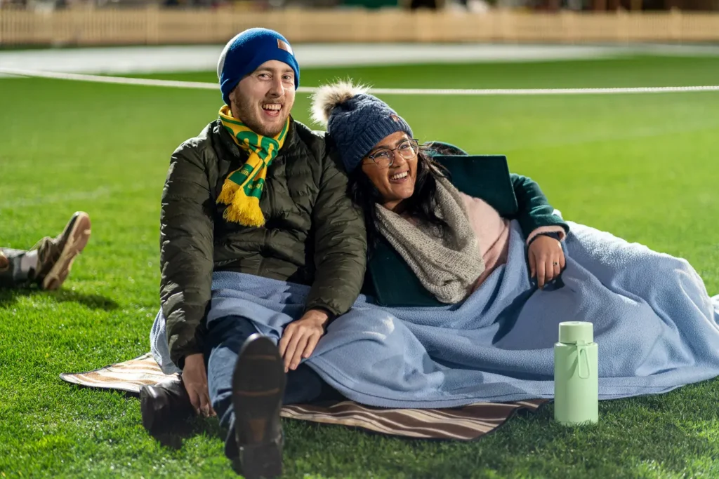 Couple wrapped in a blanket watching the Matildas match at North Sydney Oval live site
