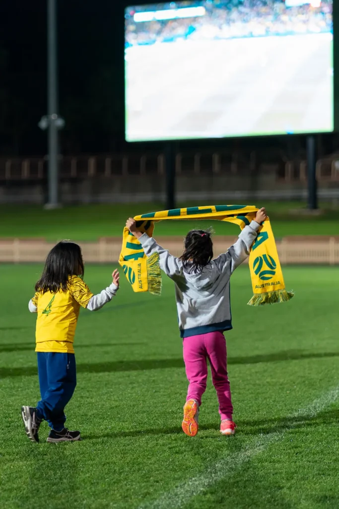 Children holding up an Australia scarf while watching the Matildas live site at North Sydney Oval
