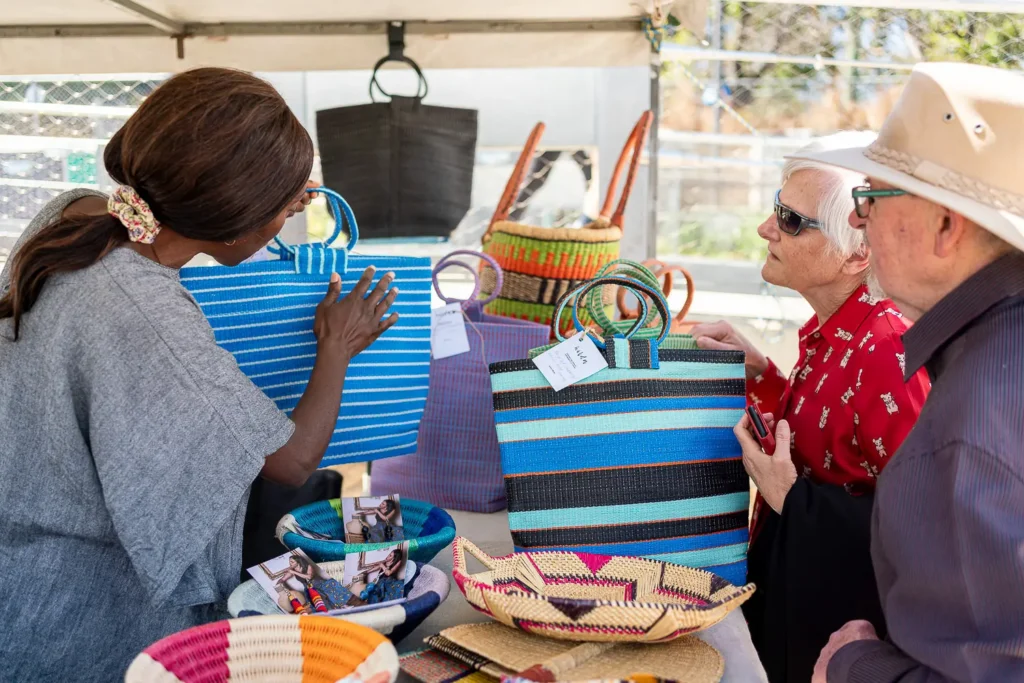 Visitors browsing colourful handmade bags at a sustainable market stall at the Coal Loader festival