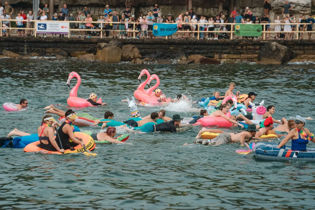 Participants racing across the water on colourful flamingo inflatables at Manly