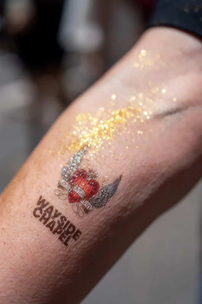 Close-up of a glittery Wayside Chapel Christmas tattoo on an arm
