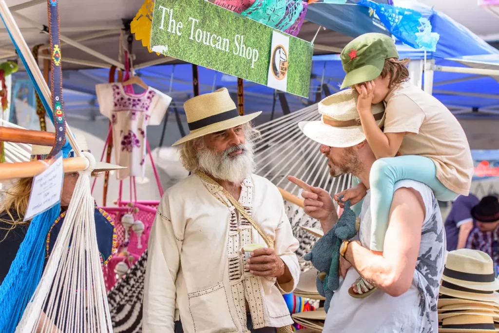 Father carrying his child while chatting with a market stallholder at Glebe Street Fair Sydney