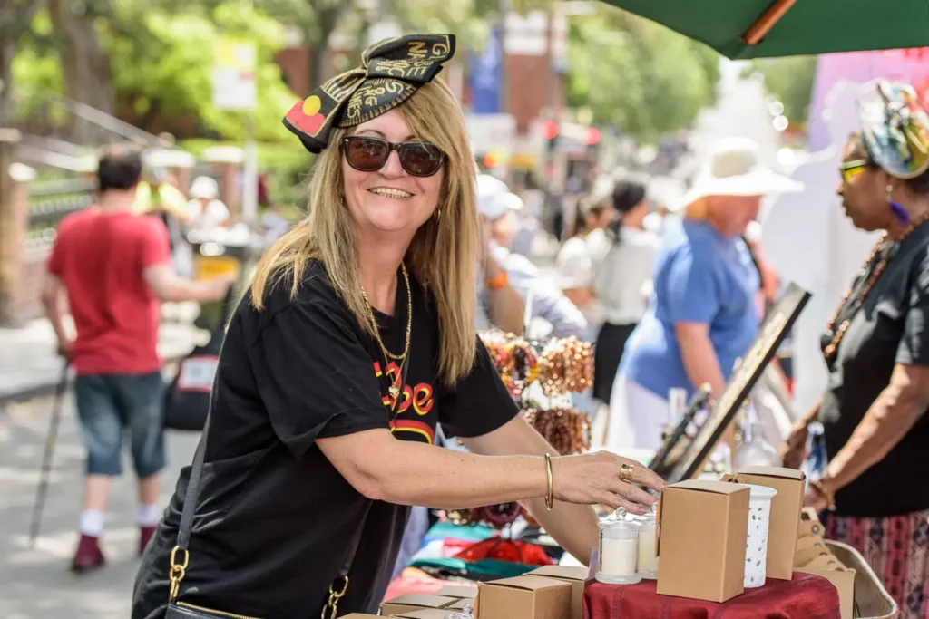 Smiling market stallholder wearing an Aboriginal flag accessory at Glebe Street Fair Sydney