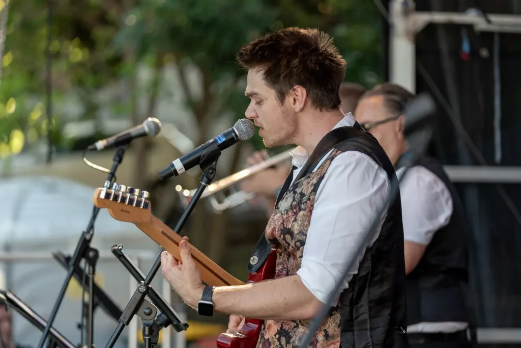 Guitarist singing into a microphone during an outdoor live music performance in North Sydney
