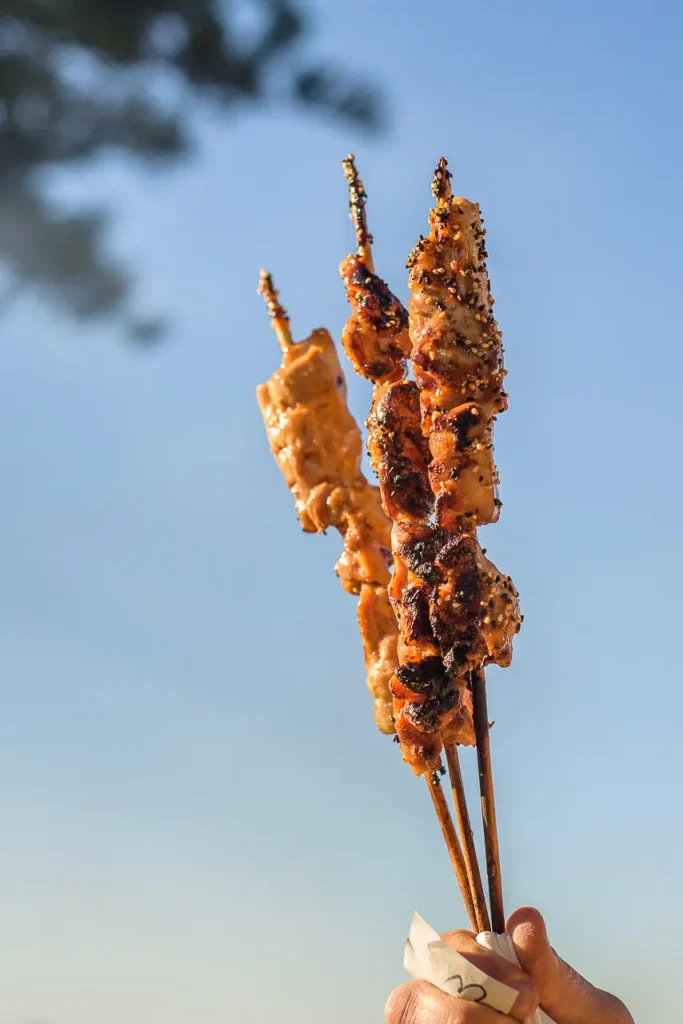 Grilled meat skewers held up against the blue sky at Taste of Manly